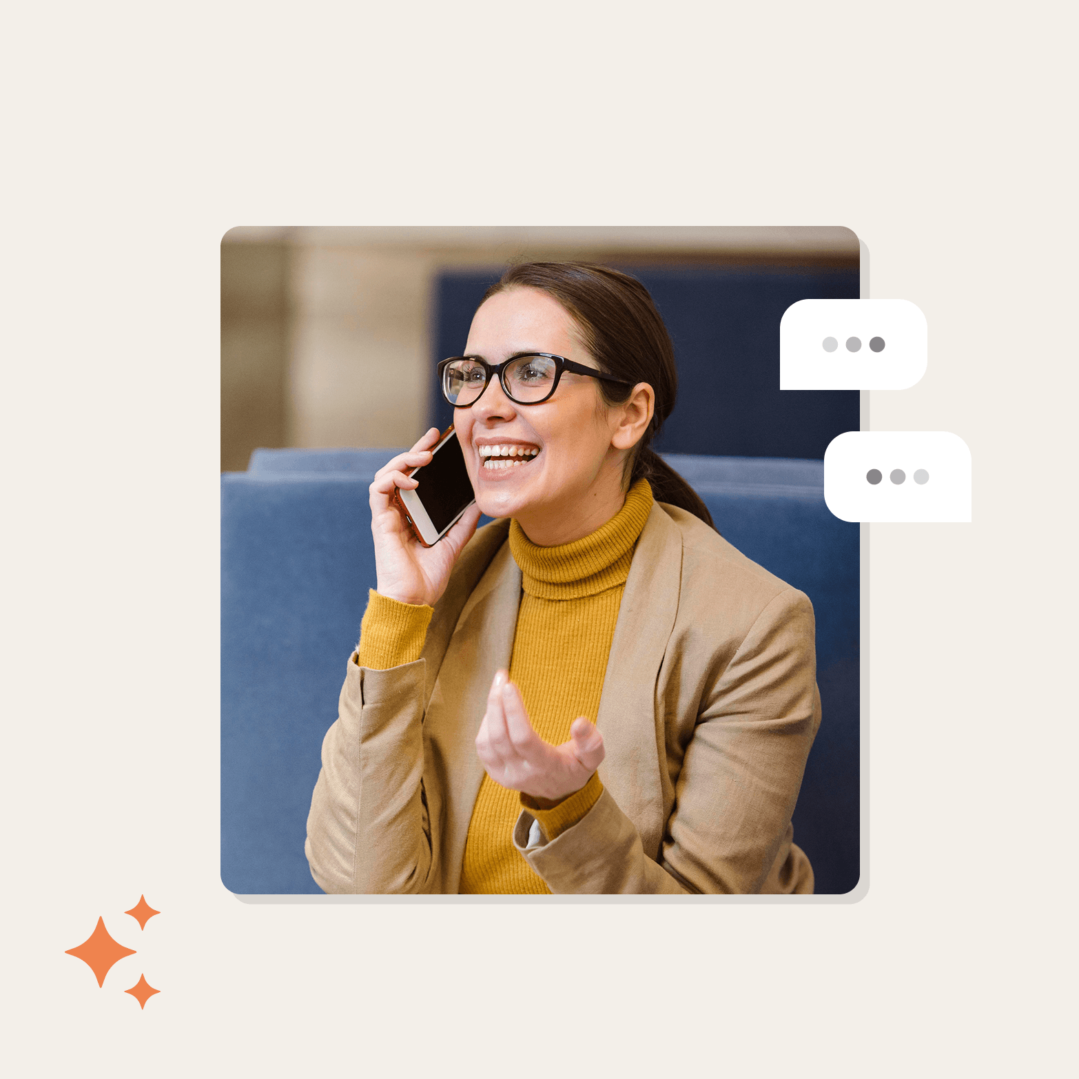 A smiling woman with glasses talks on a smartphone while gesturing expressively, seated on a blue sofa in an office setting. Two white speech bubble icons with ellipsis dots appear to her right, and an orange sparkle icon sits in the lower left corner, all on a light cream background.
