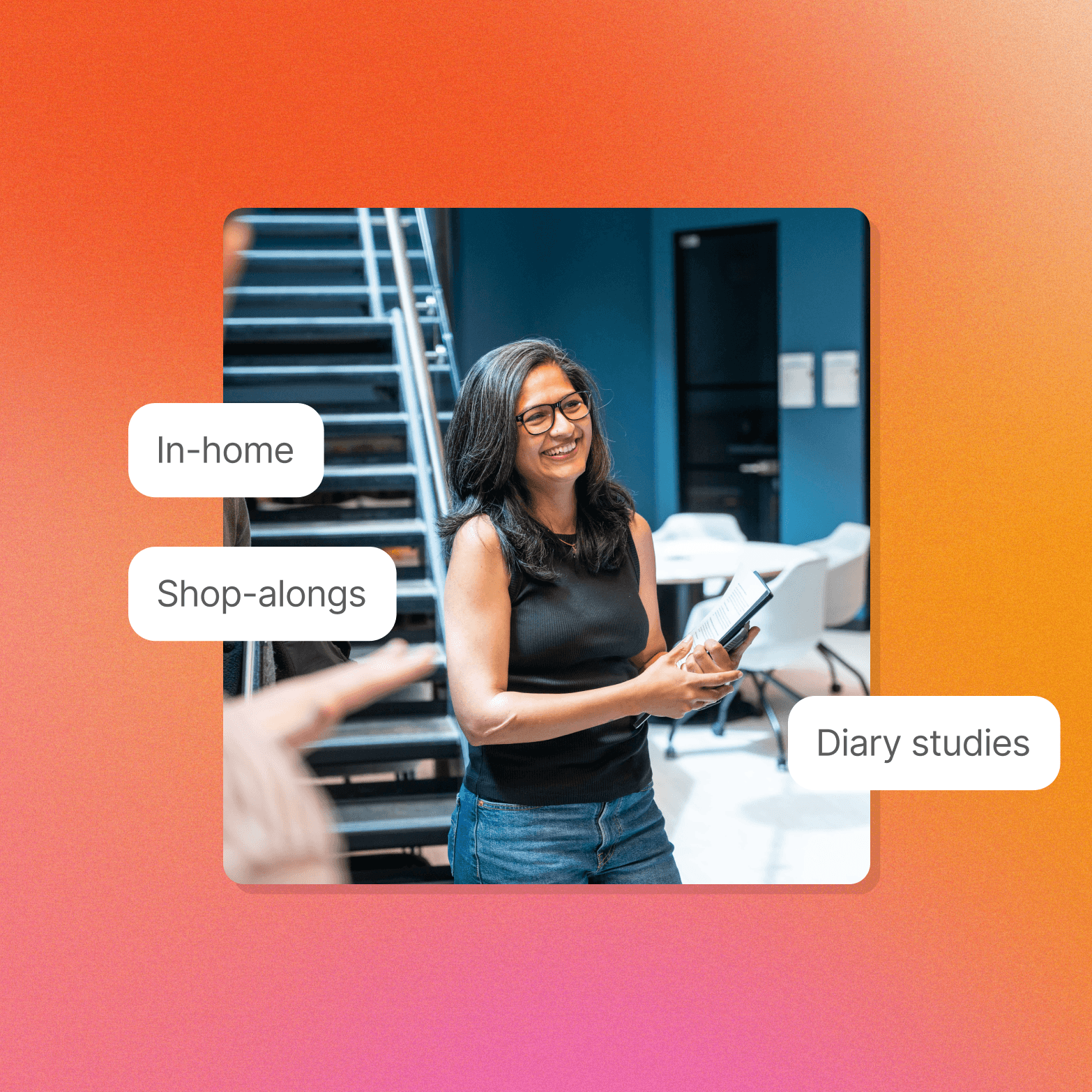 Photo of a smiling woman with glasses holding a notebook and pen in an office setting with a spiral staircase, with white callout labels reading "In-home," "Shop-alongs," and "Diary studies" placed around the image on an orange-to-pink gradient background.