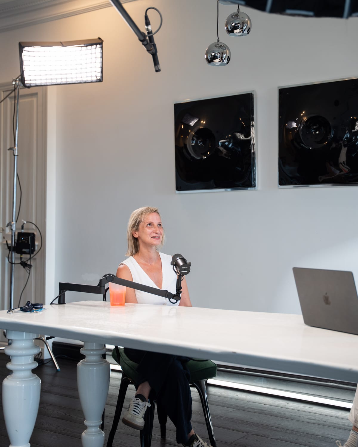 Angeliki Maragkou smiling at the microphone beneath studio lights and softboxes on the Conveo podcast set at Cannes Lions 2026