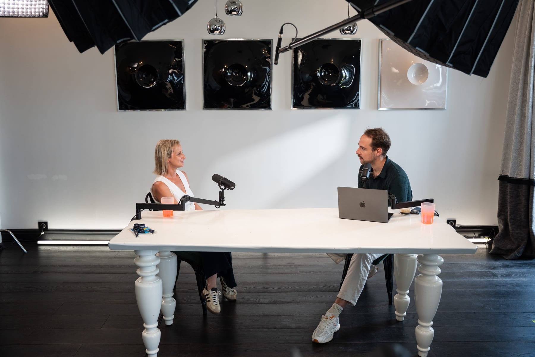 Wide shot of Angeliki Maragkou and Tom Husson facing each other across the white podcast table at Cannes Lions 2026