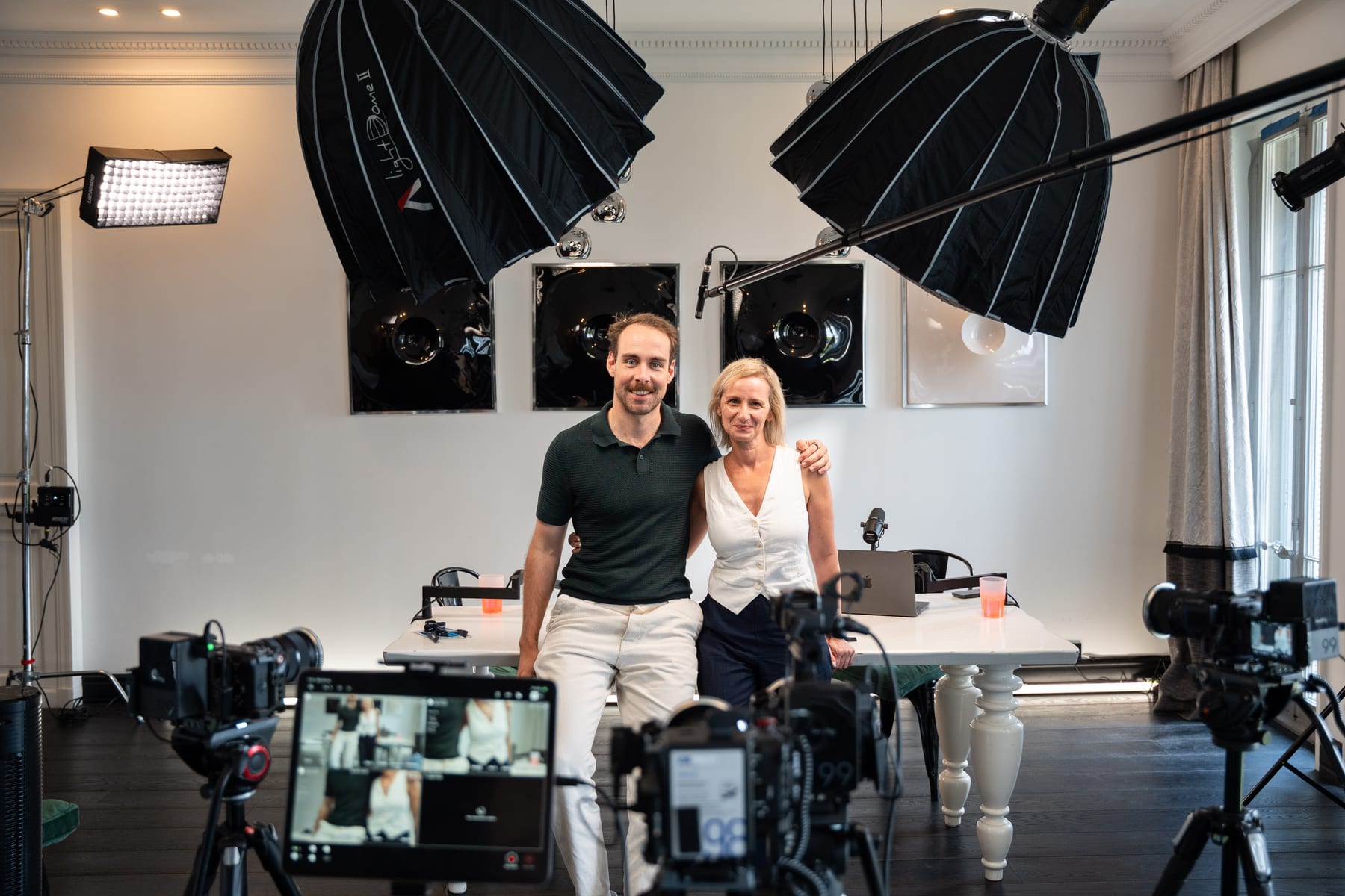 Tom Husson and Angeliki Maragkou posing arm in arm in front of the podcast table, framed by softboxes and cameras at Cannes Lions 2026