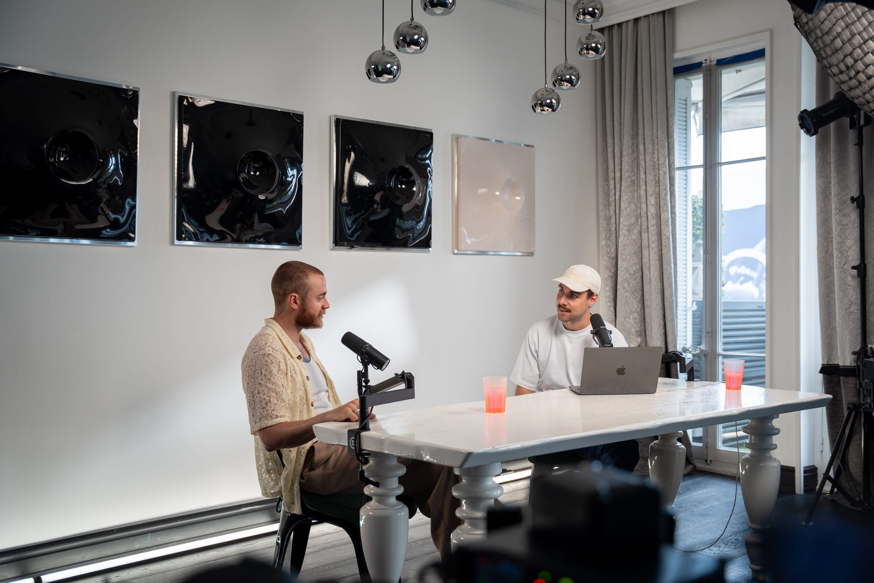 Brock Johnson and the host talk across a white table with microphones and a laptop on the Conveo podcast set at Cannes Lions 2026.