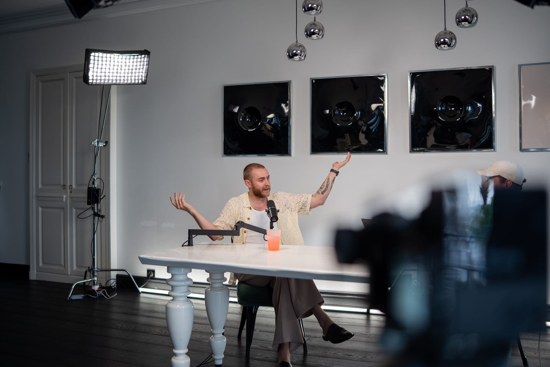 Brock Johnson spreads his arms wide mid-answer at the podcast table, with a camera rig in the foreground, at Cannes Lions 2026.
