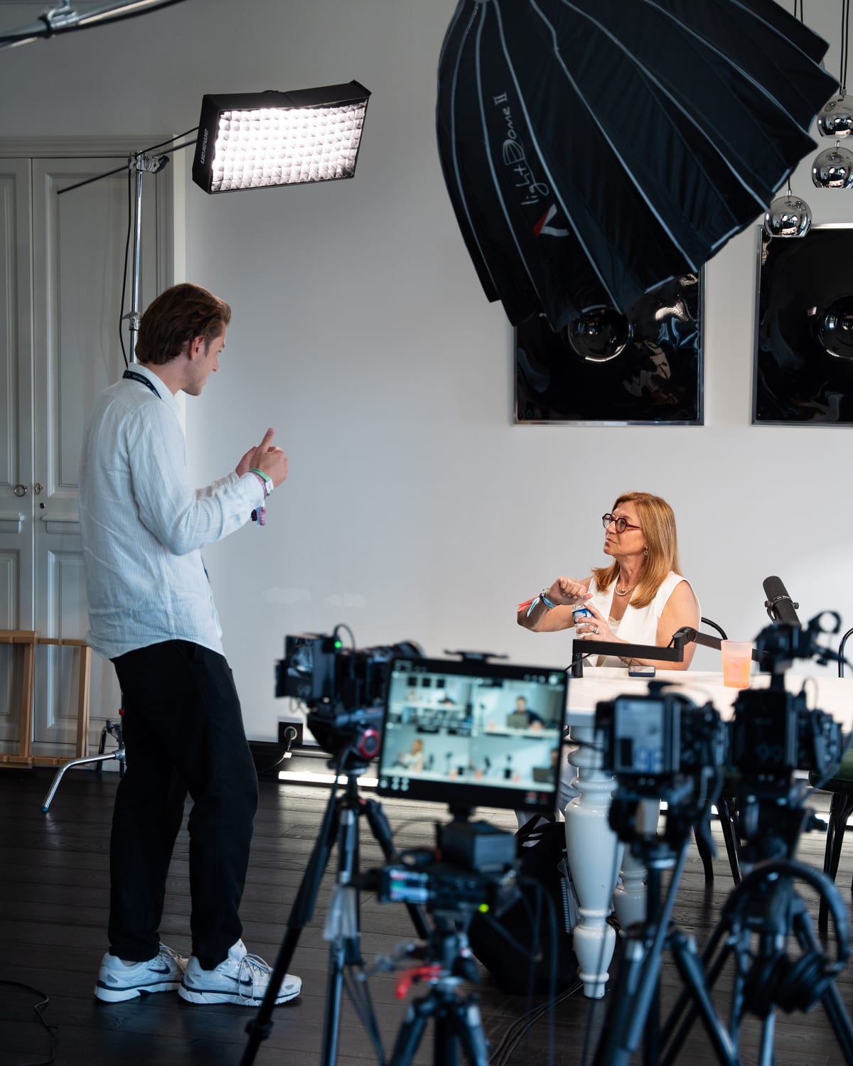 Carole Irgang gestures as she talks with a crew member beside the cameras and lights of the Conveo podcast set at Cannes Lions 2026.