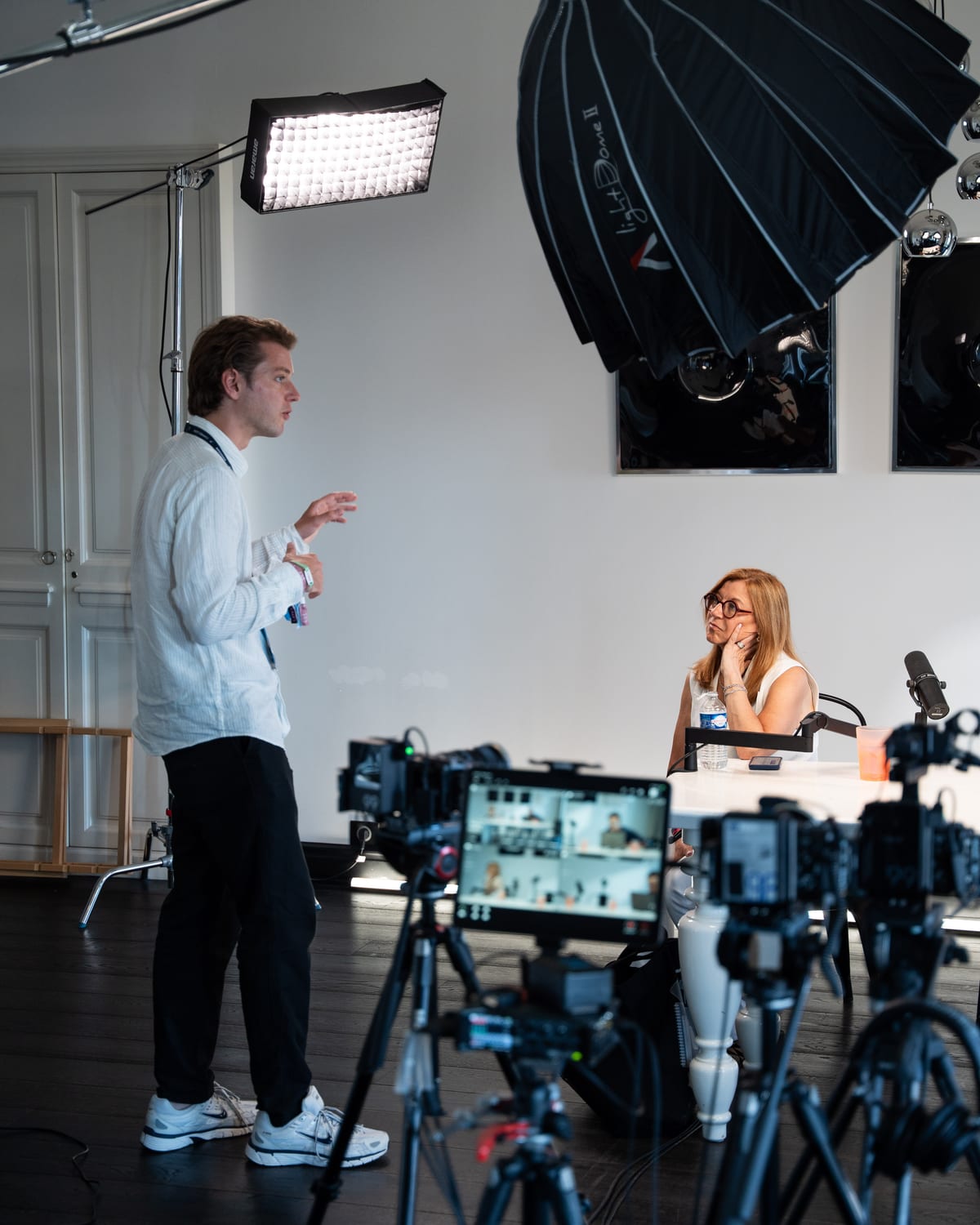 Carole Irgang rests her hand at her chin while a standing crew member talks with her on the Conveo podcast set at Cannes Lions 2026.
