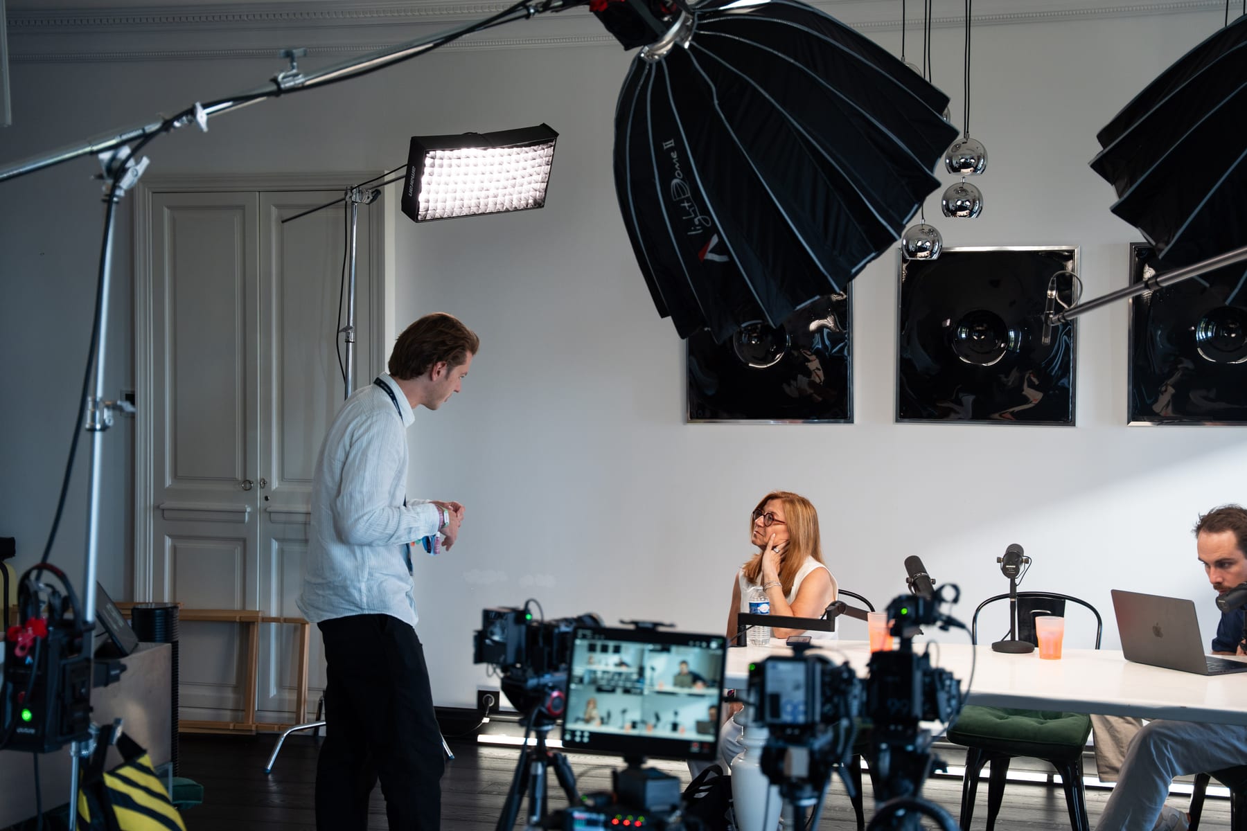 Wide view of the Conveo podcast studio, with Carole Irgang seated at the table, a crew member standing by the lights and a second crew member at a laptop at Cannes Lions 2026.