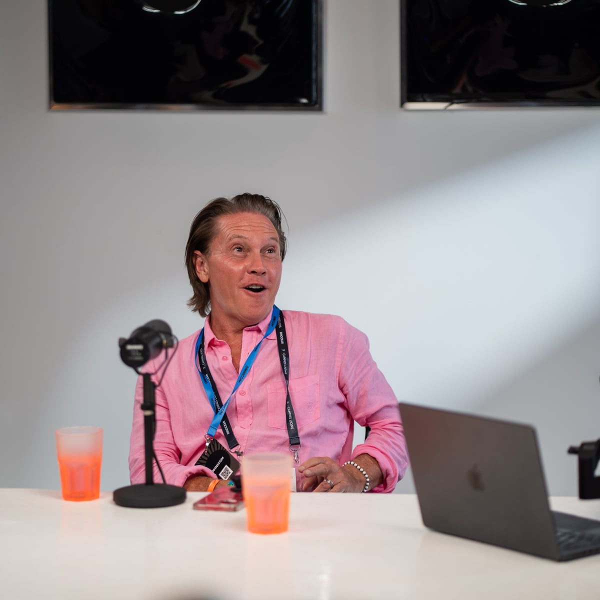 Christopher Nurko in a pink shirt and festival lanyard at the microphone on the Conveo podcast set at Cannes Lions 2026