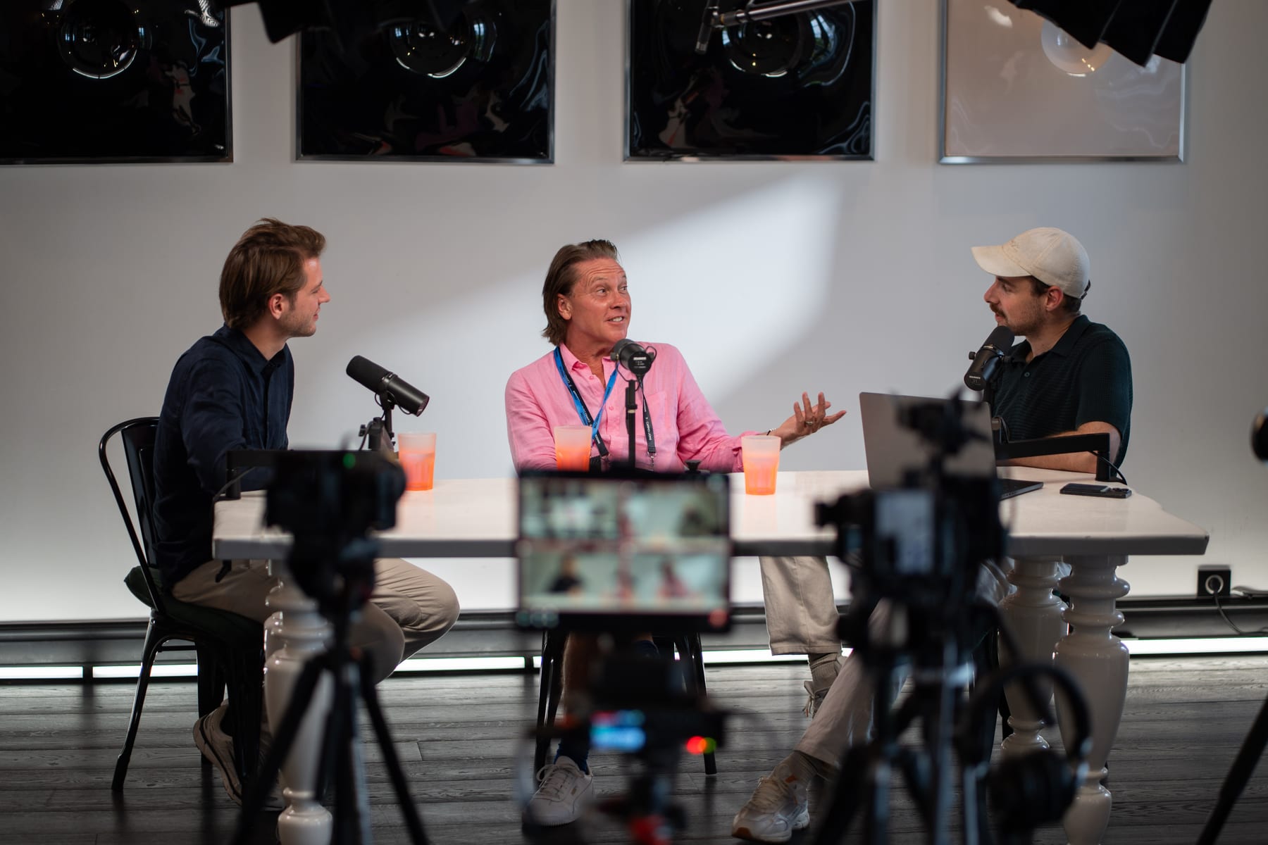 Christopher Nurko gestures with both hands while two hosts face him on the Conveo podcast set, framed between video cameras at Cannes Lions 2026.