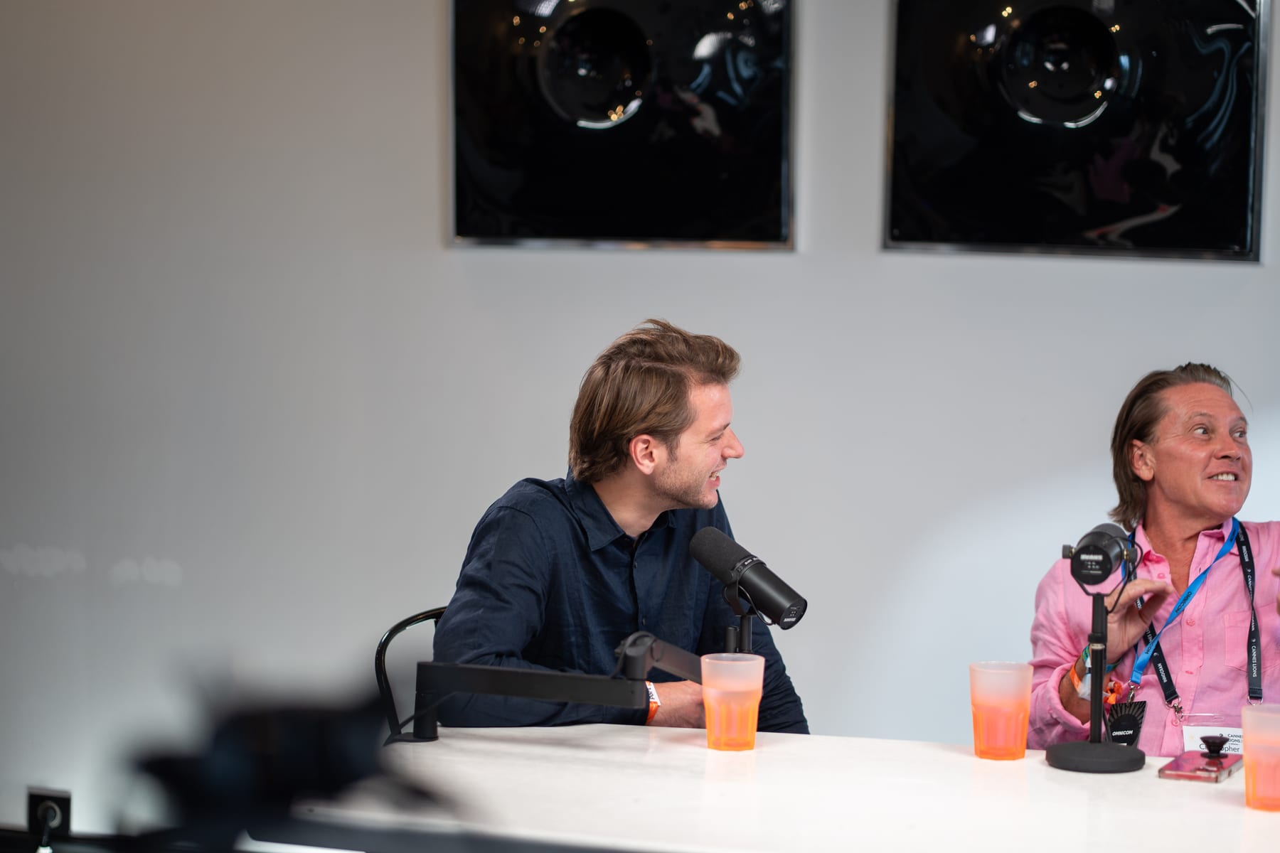 A host in a navy shirt laughs beside Christopher Nurko, who smiles at his microphone on the Conveo podcast set at Cannes Lions 2026.
