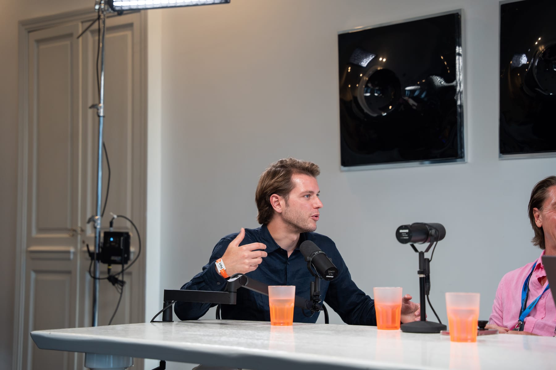 A host in a navy shirt gestures as he asks a question at the microphone, with Christopher Nurko at the edge of the frame, at Cannes Lions 2026.