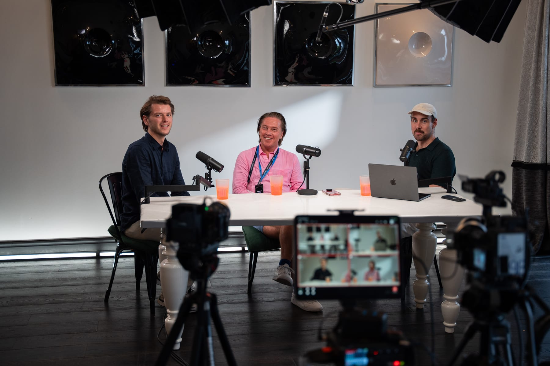 Christopher Nurko and the two Conveo hosts smile toward the camera at the podcast table, with cameras and a monitor in the foreground at Cannes Lions 2026.