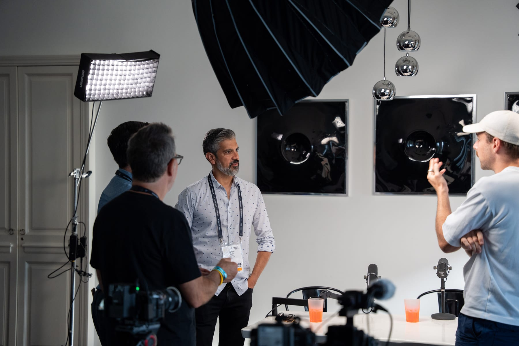 Barry Wacksman, Saneel Radia and the host chat with the crew beside the microphones on the Conveo podcast set before recording at Cannes Lions 2026.