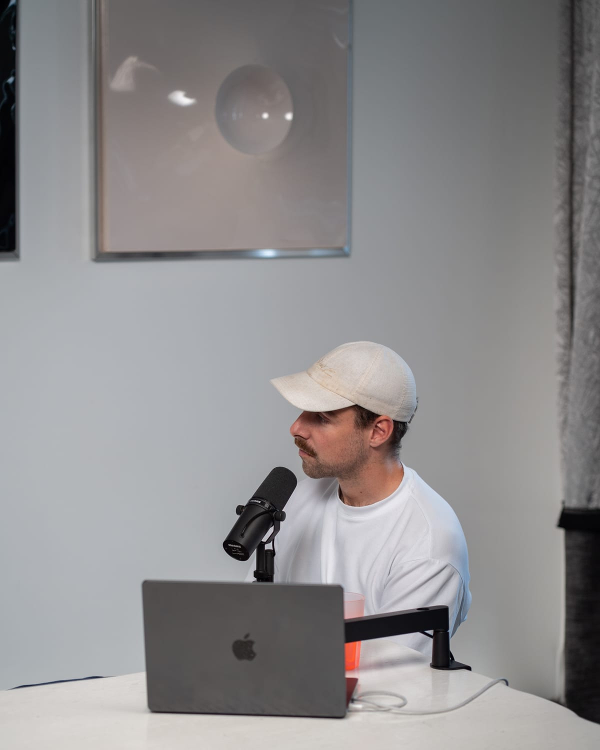 The host, in a white cap, speaks into a microphone behind a laptop on the Conveo podcast set at Cannes Lions 2026.