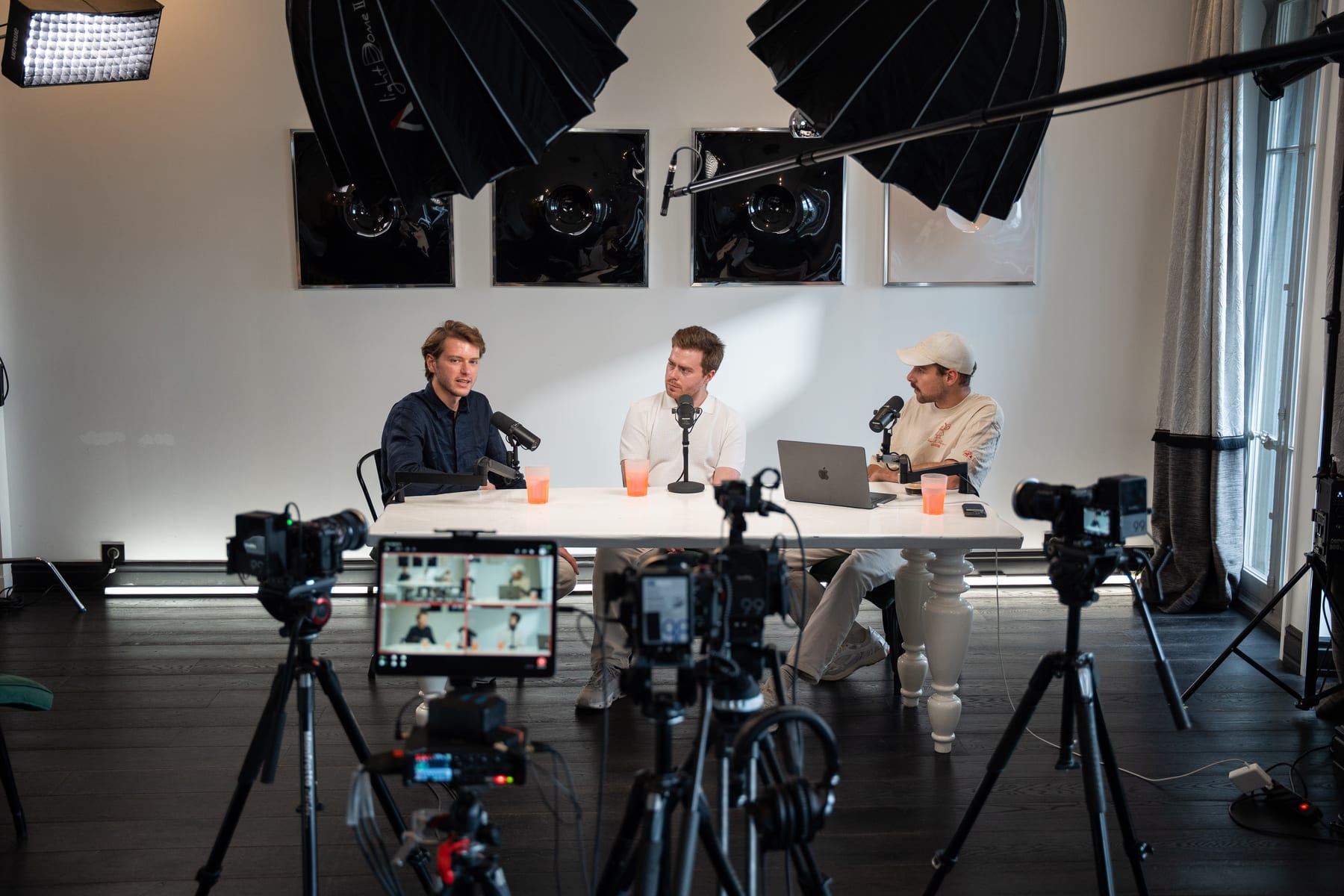 Wide view of the Conveo podcast studio, with softbox lights, cameras and a preview monitor framing Hendrik Van Hove, Doug Tallmadge and a third person in a cap at the table at Cannes Lions 2026