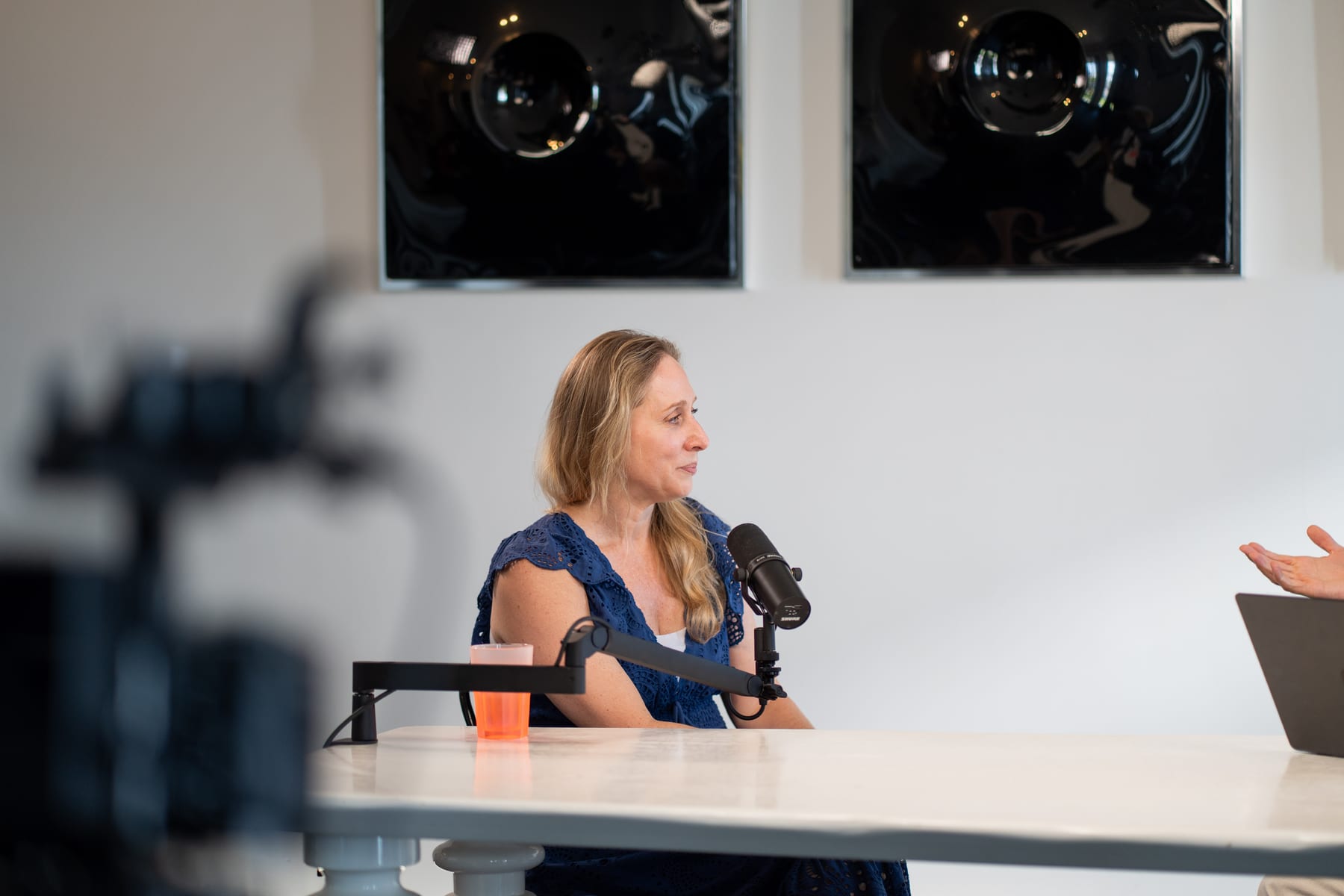 Karen Ehrlich speaking into a microphone at the podcast table, with a blurred camera rig in the foreground, at Cannes Lions 2026