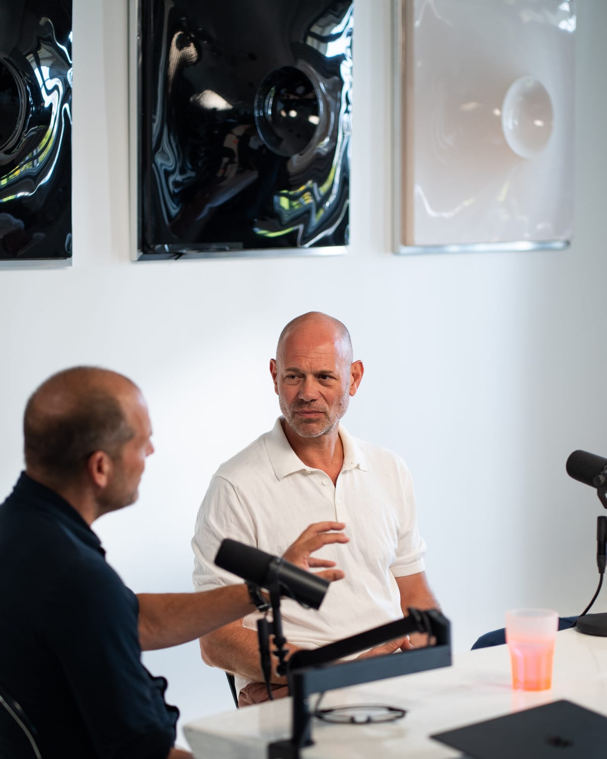 Niels Schillewaert in a white polo looks across the table as Kees Kruythoff, seen from behind, gestures on the Conveo podcast set at Cannes Lions 2026