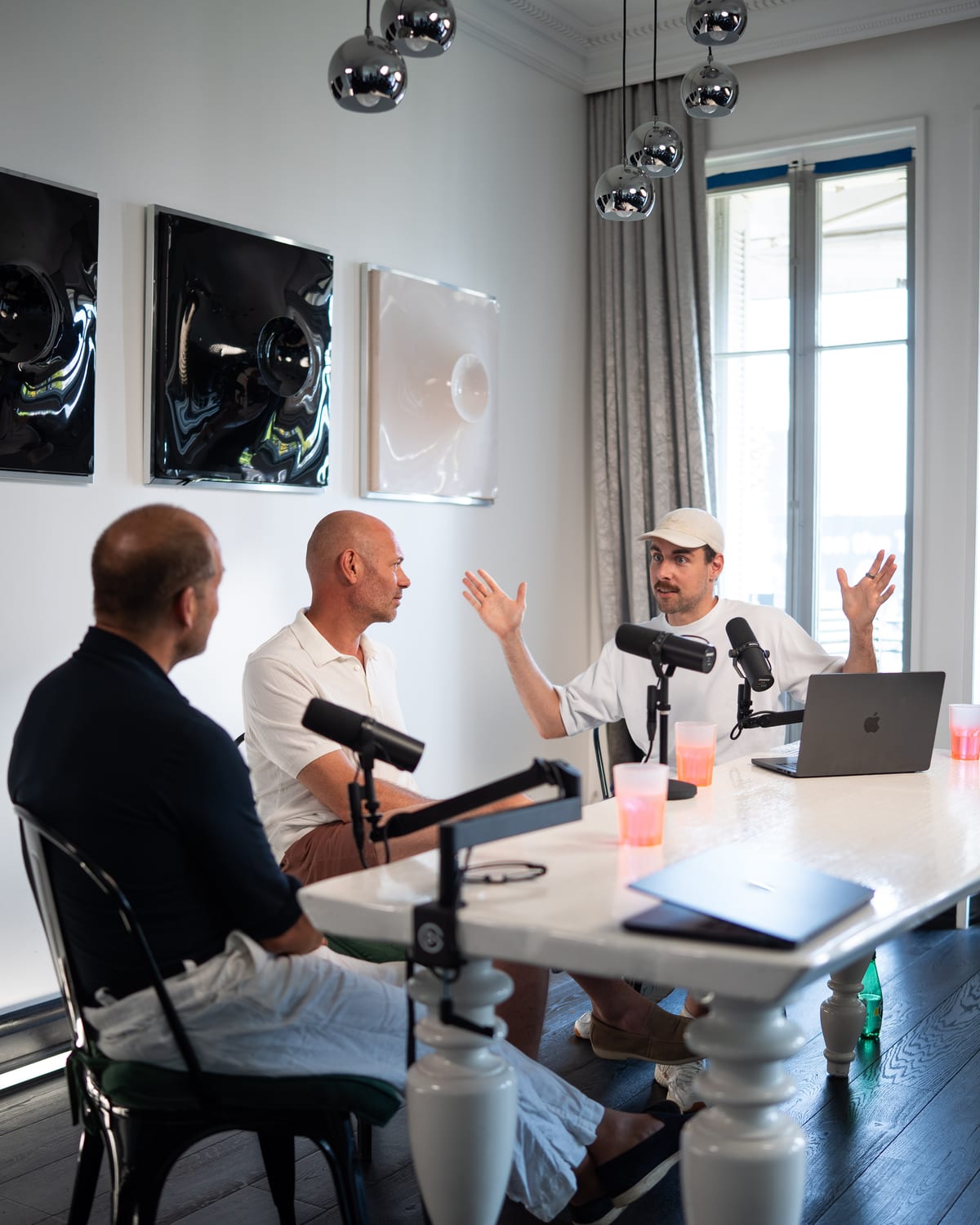 Host Tom Husson raises both hands mid-question while Niels Schillewaert and Kees Kruythoff face him at the podcast table at Cannes Lions 2026