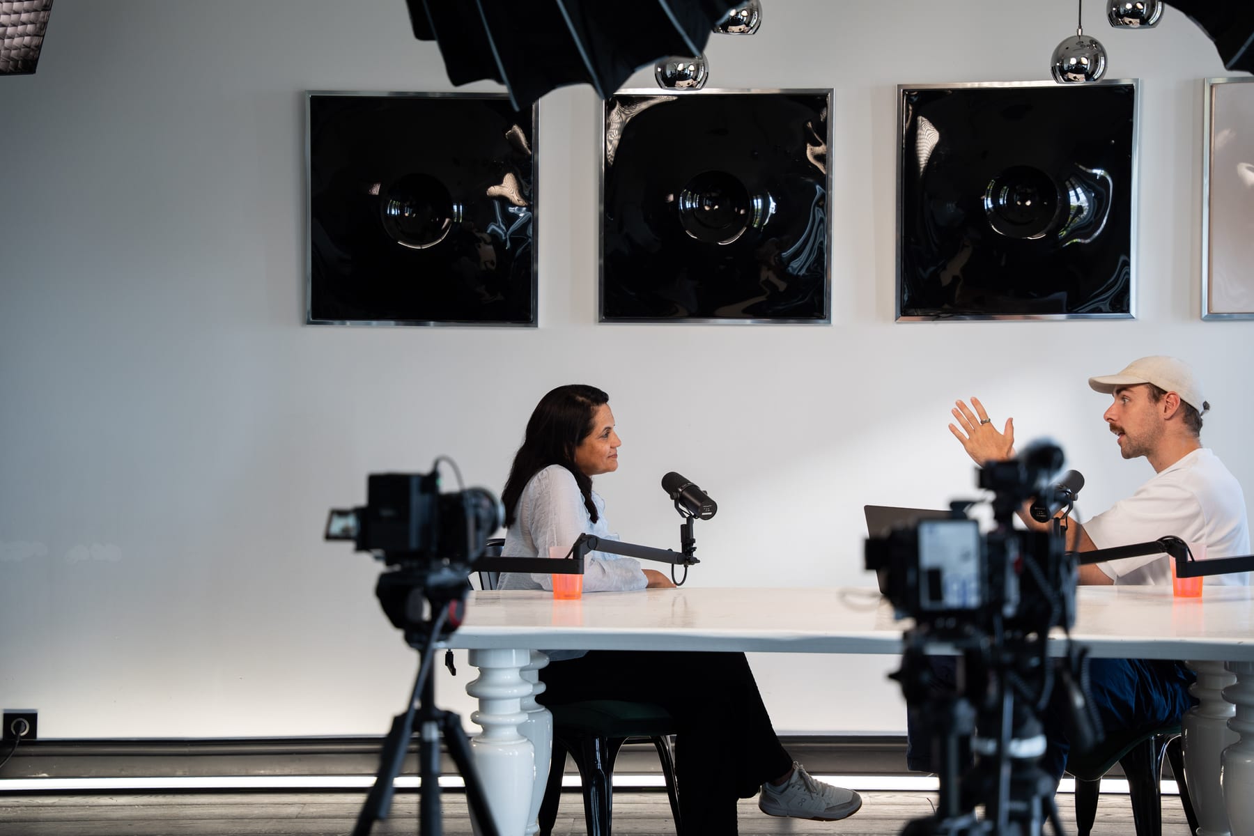 The Conveo host gestures mid-question while Lulu Raghavan sits across the table between camera rigs at Cannes Lions 2026.
