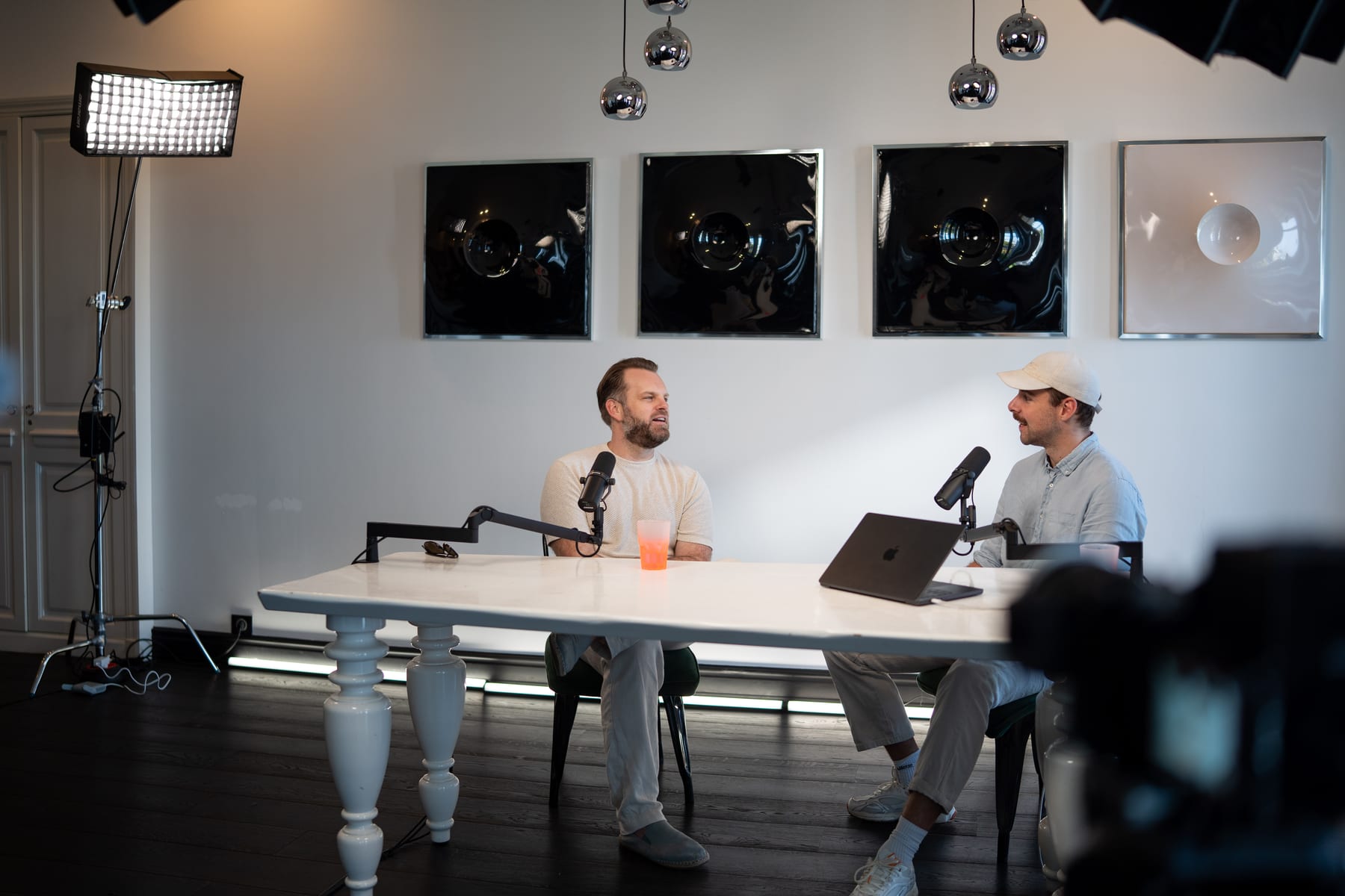 Matt Hammel and the host talk across the white podcast table, with an LED panel light and the studio's black wall art behind them at Cannes Lions 2026