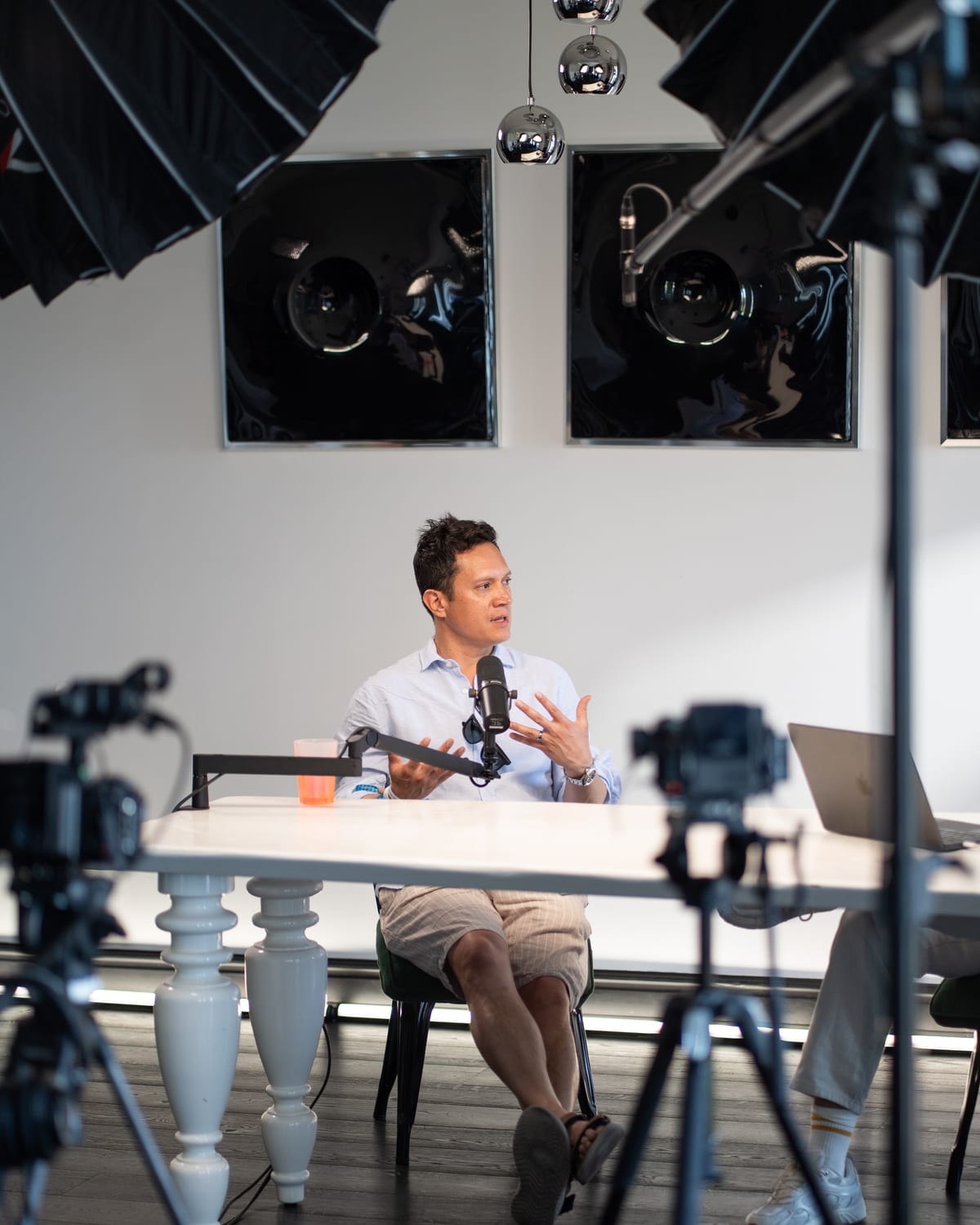 Miguel Avalos speaks into a microphone at the podcast table, framed between camera tripods on the Conveo set at Cannes Lions 2026.