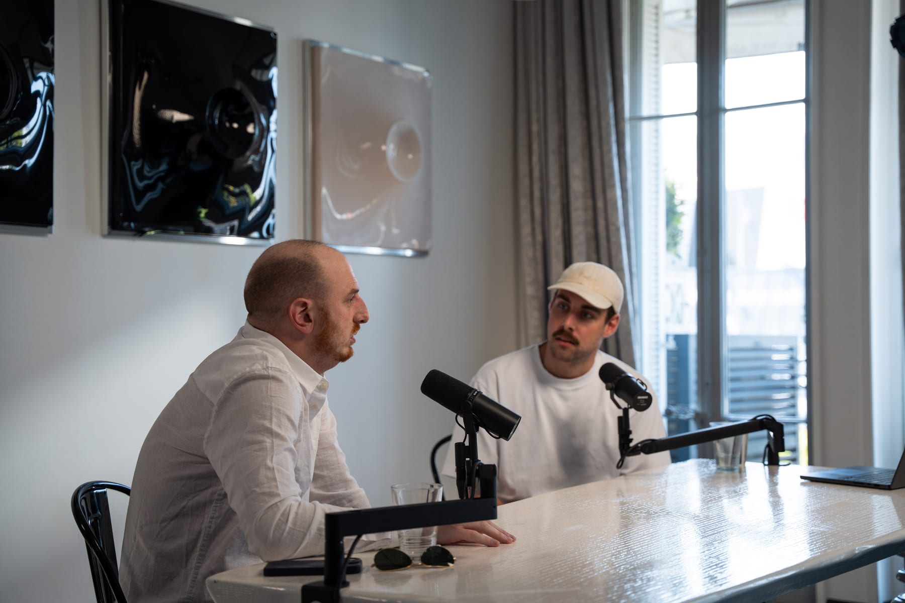 The host in a white cap faces Noah Plaue across the podcast table, seen over Plaue's shoulder, at Cannes Lions 2026