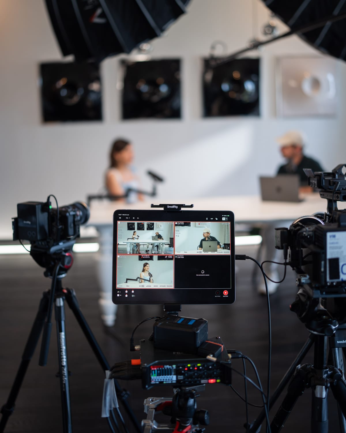A multi-camera monitor and audio recorder in the foreground show the live feeds as Özge Akcizmeci and the host talk in the background at Cannes Lions 2026
