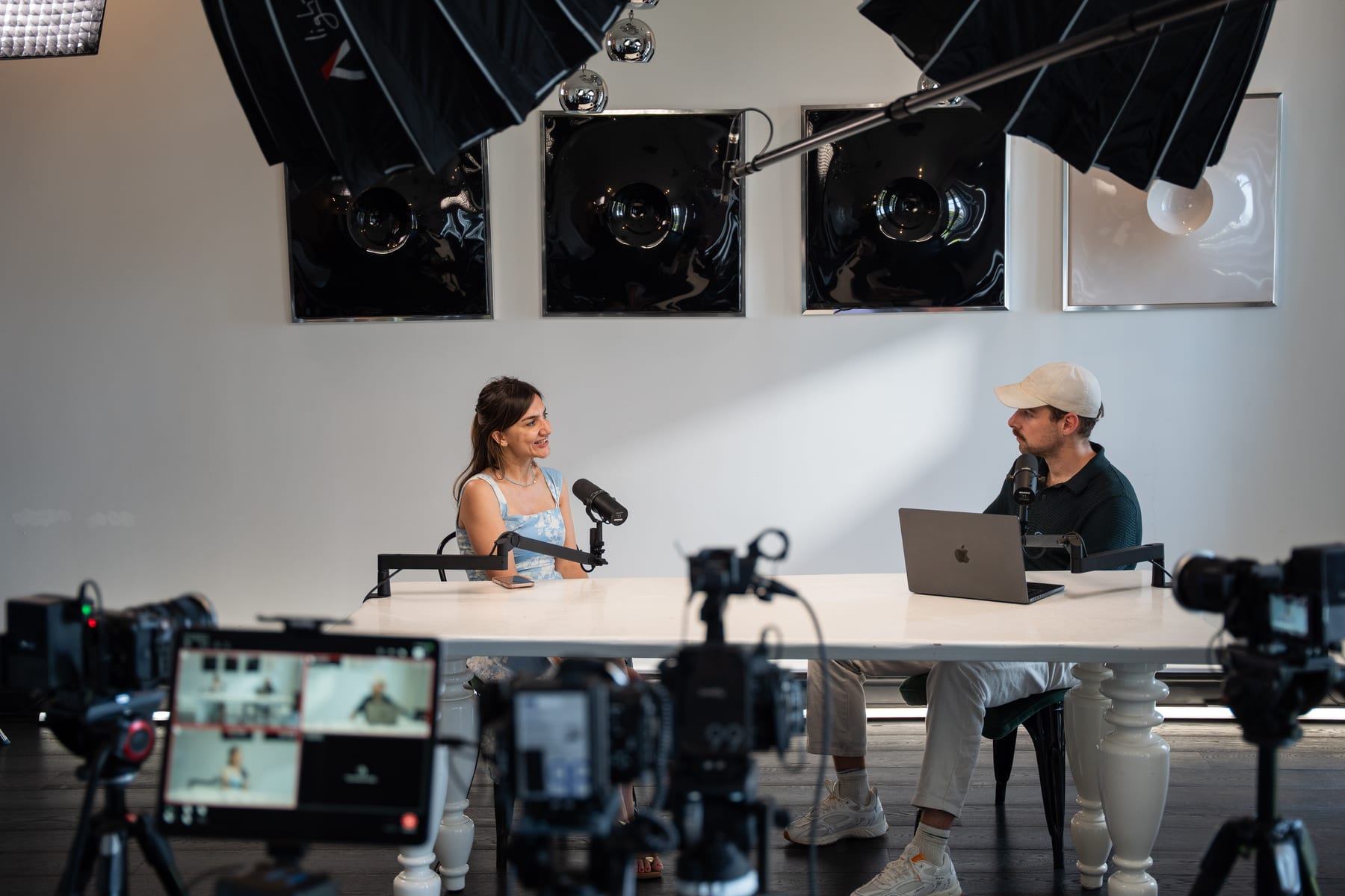 Özge Akcizmeci laughs while talking with the host, seen past a row of cameras and a monitor on the podcast set at Cannes Lions 2026