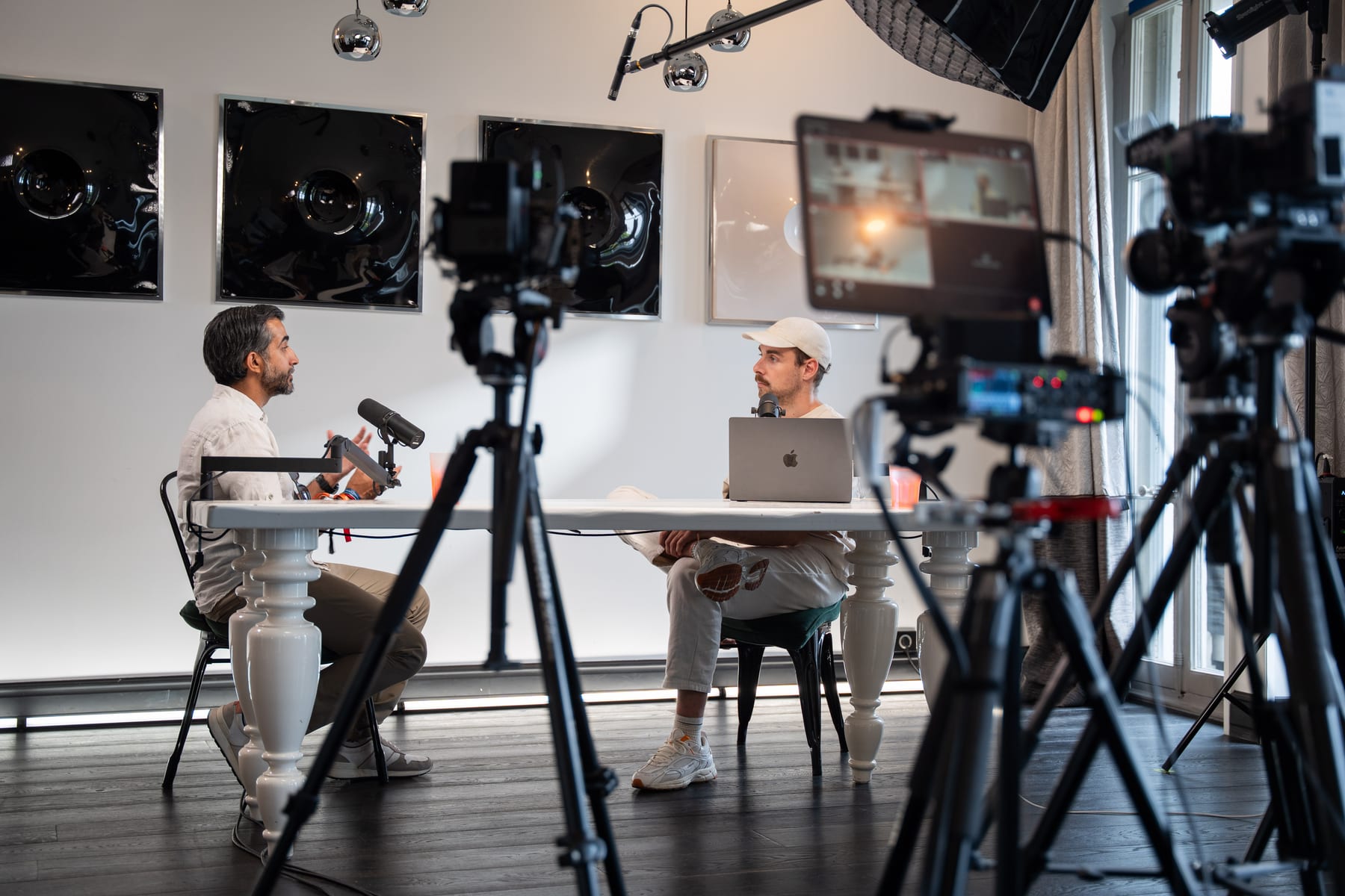 Wide view of the Conveo podcast set with Ravi Rabheru talking to the host across a white table, framed by cameras and a monitor in the foreground at Cannes Lions 2026