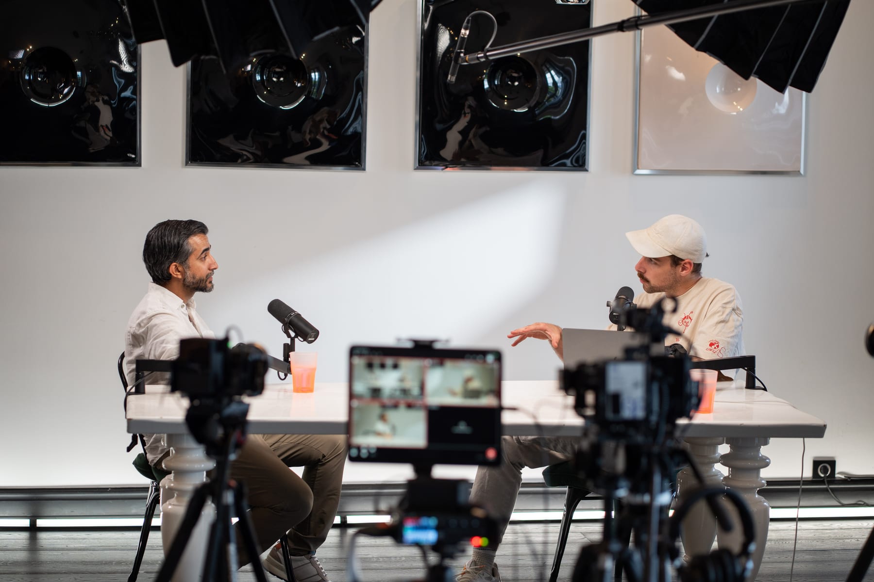 The host gestures mid-question while Ravi Rabheru faces him across the podcast table, with cameras and a monitor in the foreground at Cannes Lions 2026
