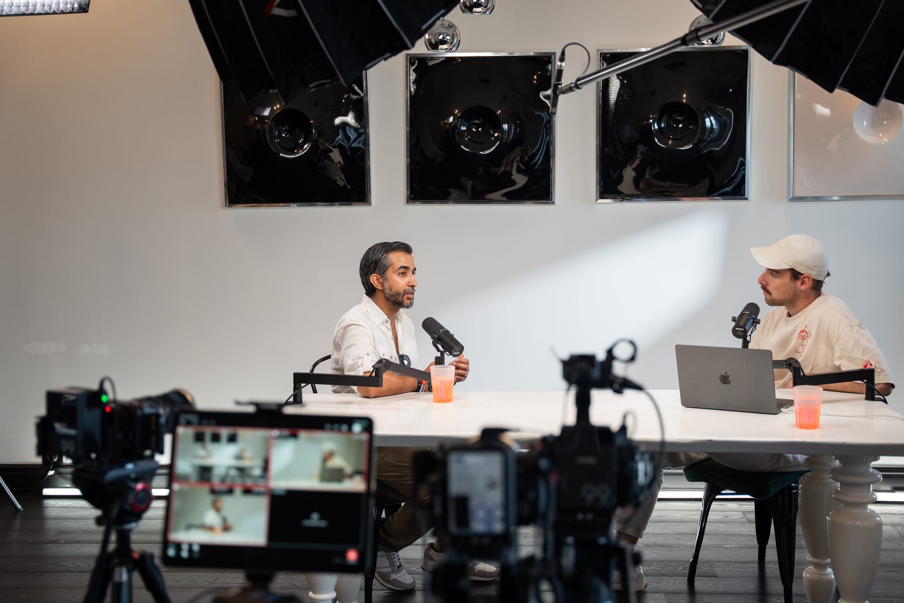 Ravi Rabheru and the host in conversation at the white podcast table, seen past camera rigs and a monitor at Cannes Lions 2026