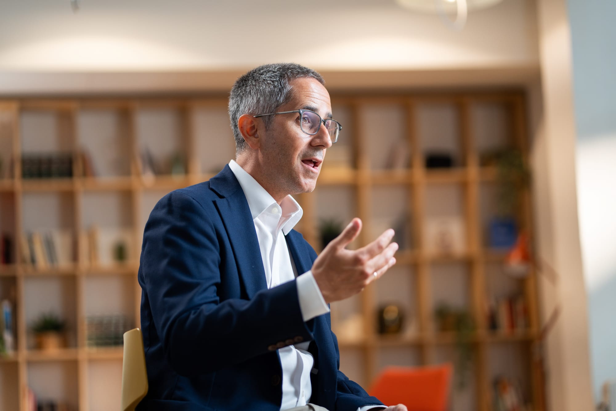 Pablo Pérez of Google gesturing mid-answer in a blue blazer and glasses, wooden bookshelves out of focus behind him.