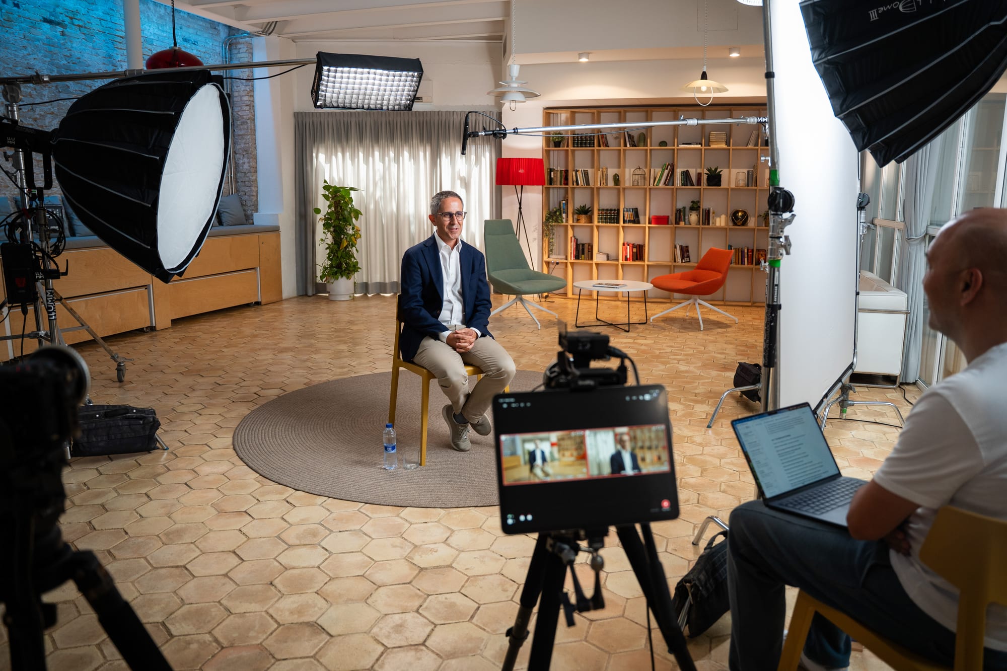 Pablo Pérez seated on a film set between softbox lights, seen past a camera monitor showing his interview and a colleague working on a laptop.