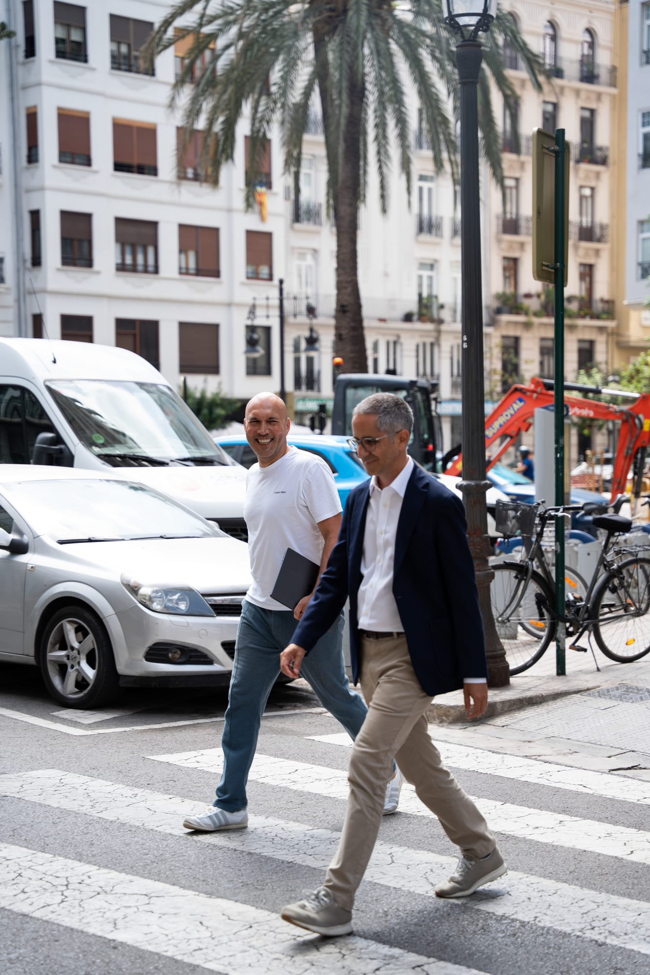 Pablo Pérez and a colleague crossing a street in Valencia, palm trees and apartment buildings behind them.